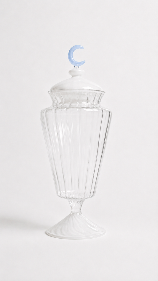 Transparent blown glass candy jar with a blue crescent moon lid inspired by traditional Ramadan fanoos lanterns, isolated on a white background.