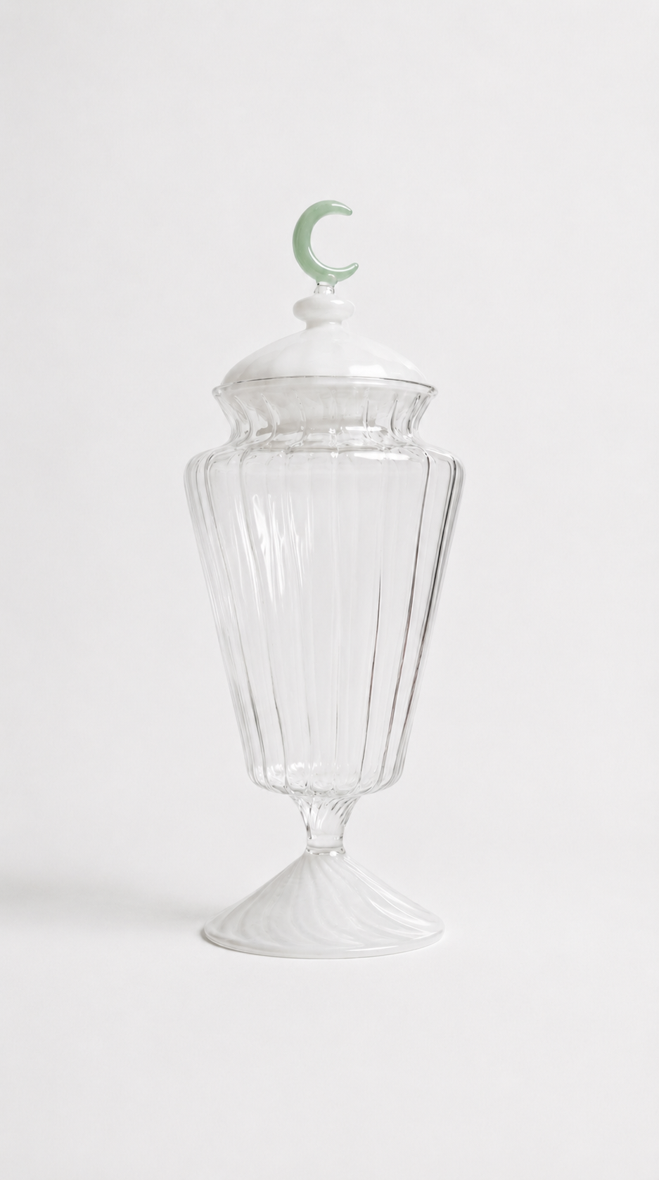 Transparent blown glass candy jar with a green crescent moon lid, inspired by traditional Ramadan fanoos lanterns, isolated on a white background.