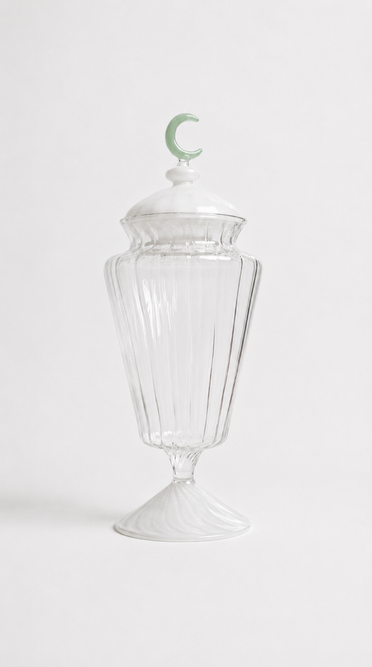 Transparent blown glass candy jar with a green crescent moon lid, inspired by traditional Ramadan fanoos lanterns, isolated on a white background.